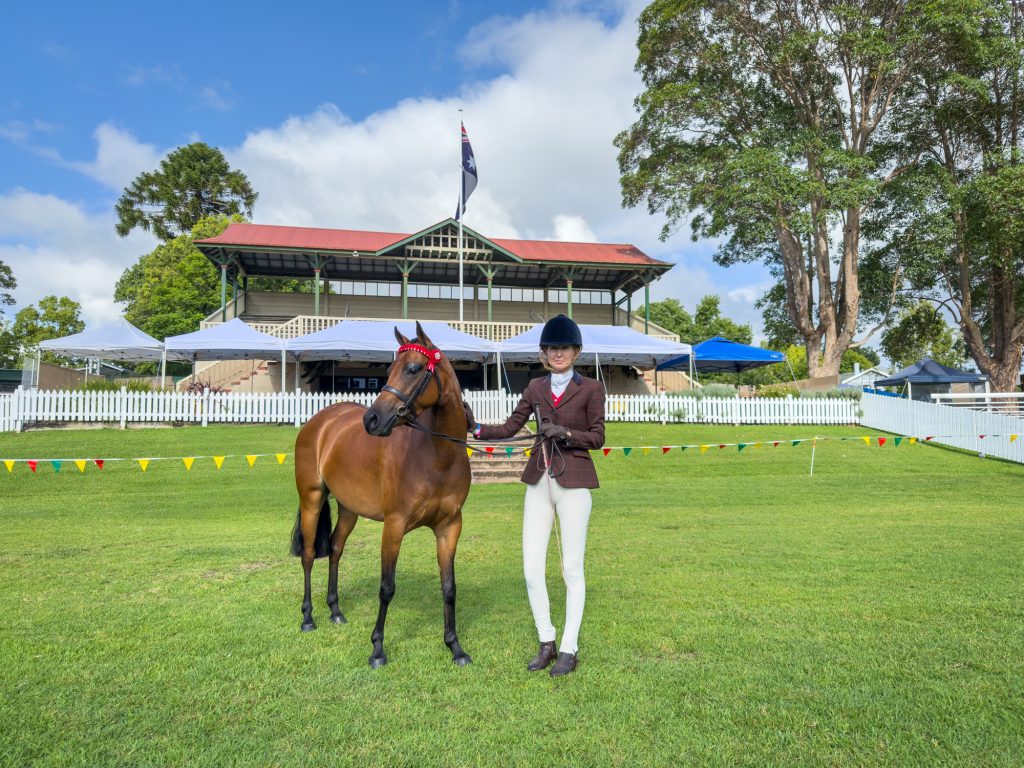 A girl standing with her pony in front of the grandstand
