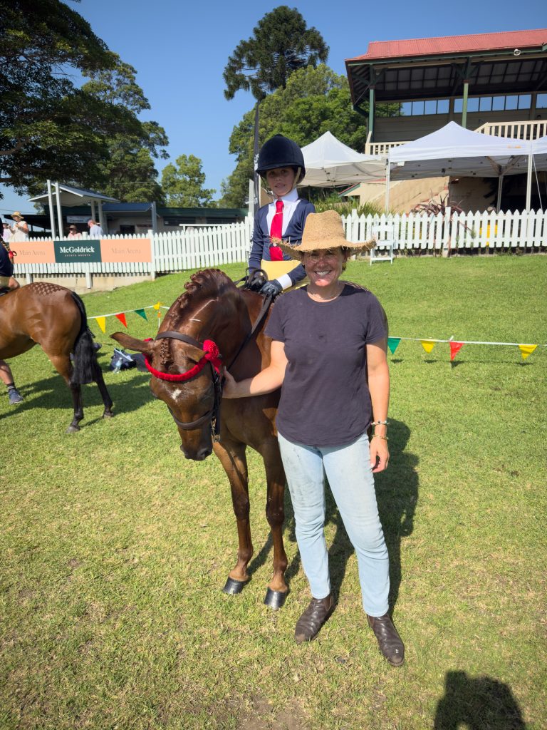 A man holding a horse with a red ribbon in front of the grandstand