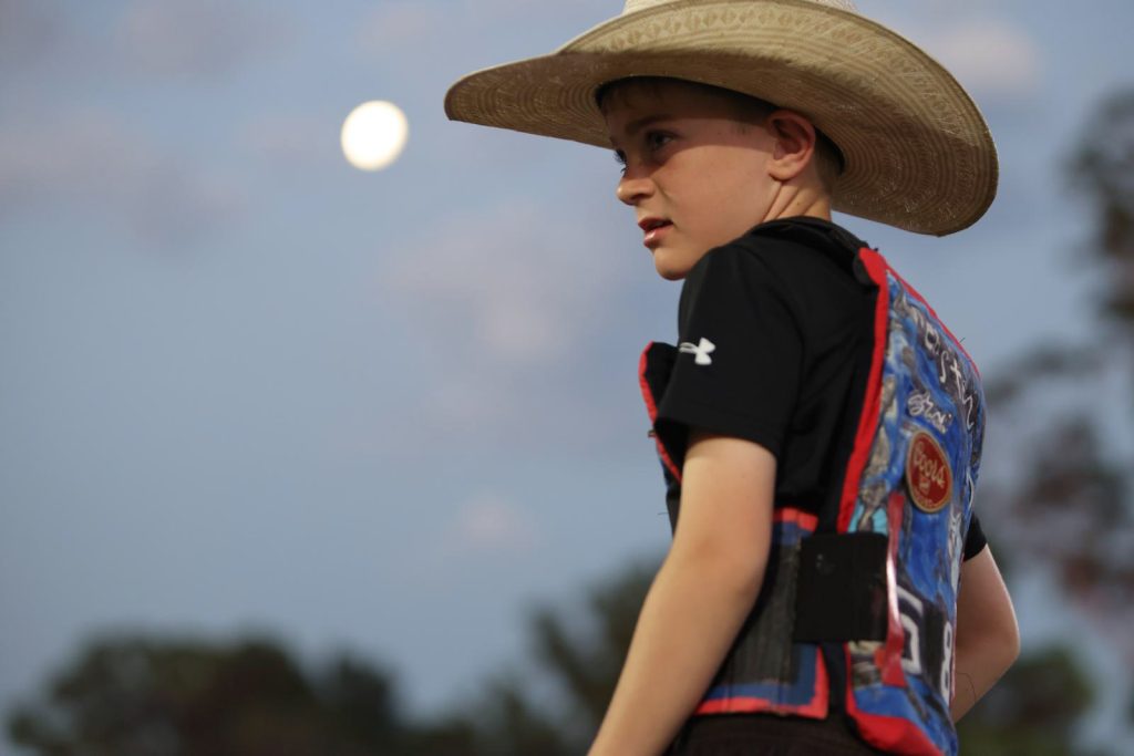 A boy in a cowboy hat and riding vest under the moon