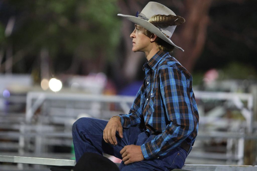 A young cowboy watching from the rails