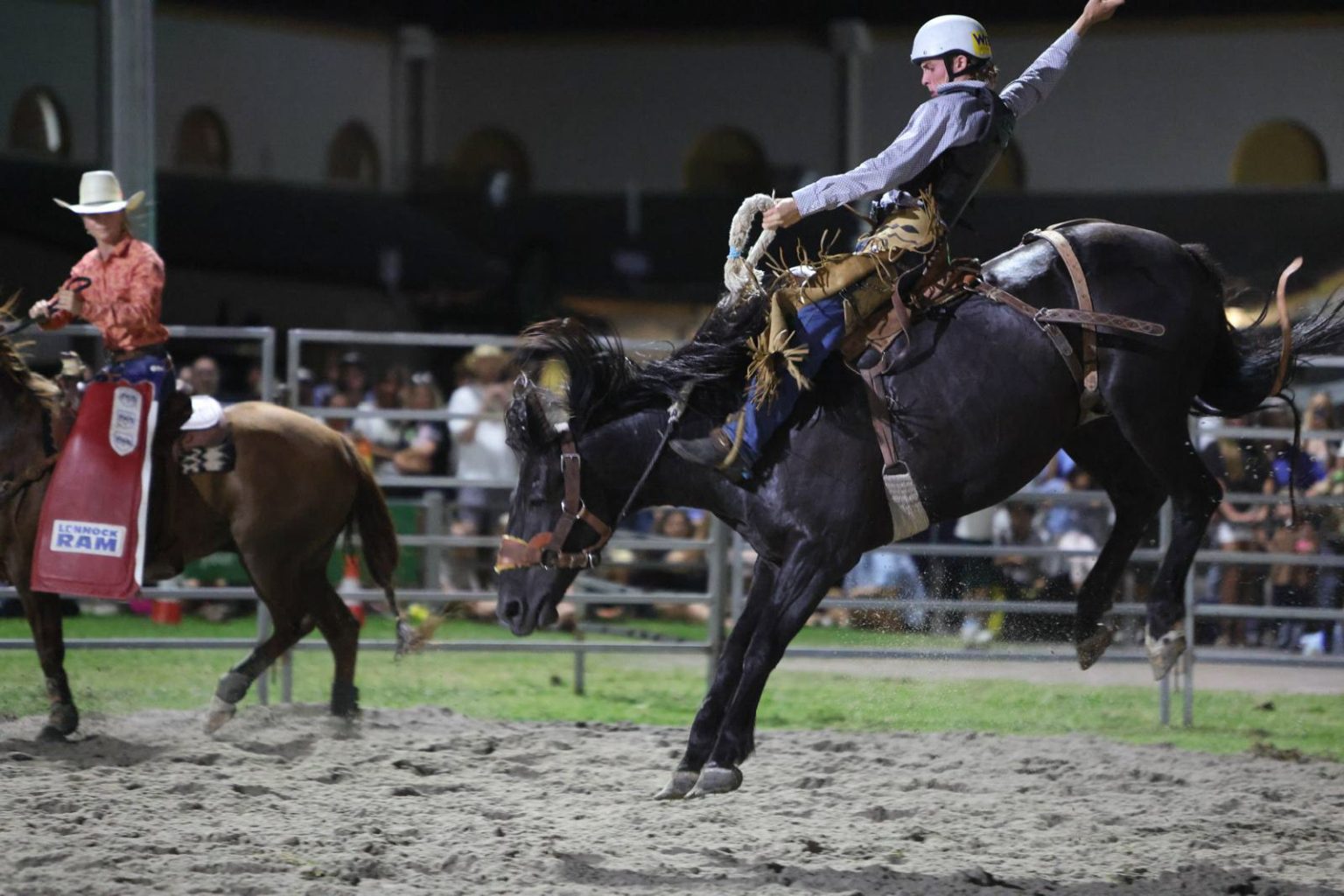A bronc rider in mid-air under the lights