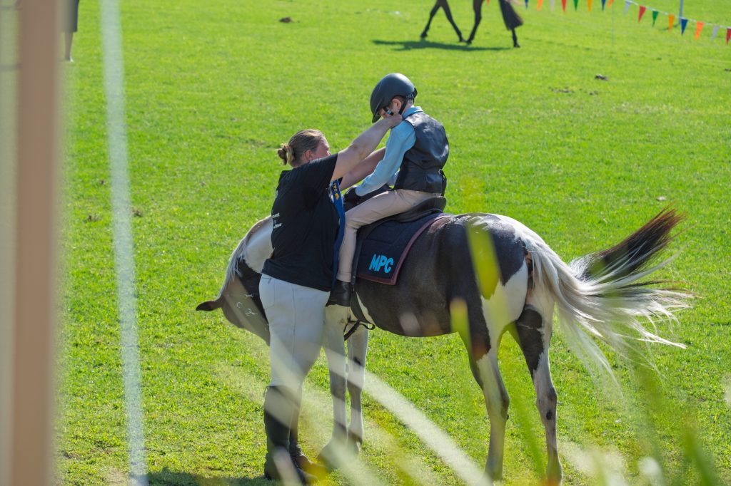 A small child riding in front of an adult on a skewbald horse