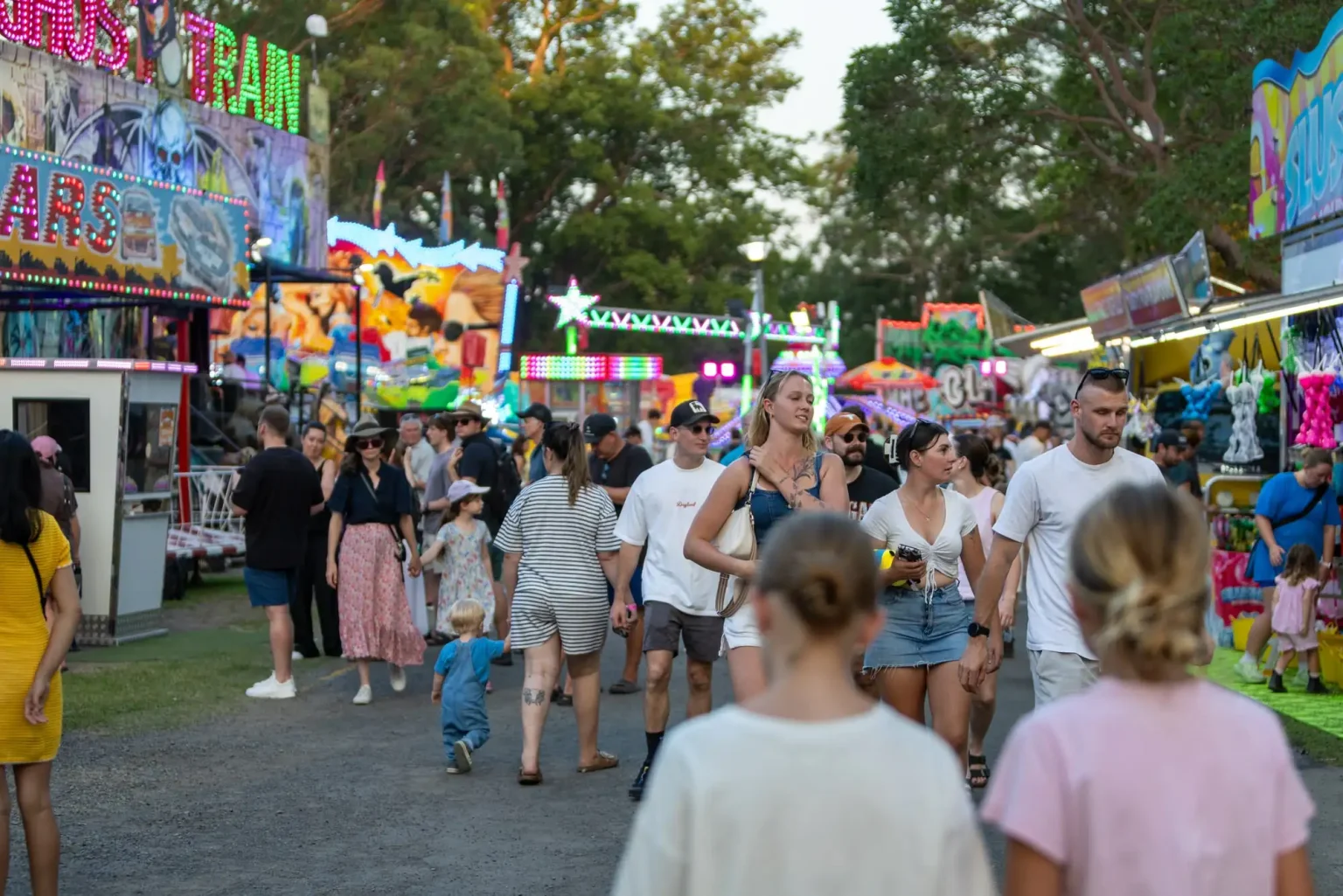 Families walking through Sideshow Alley among the rides and stalls